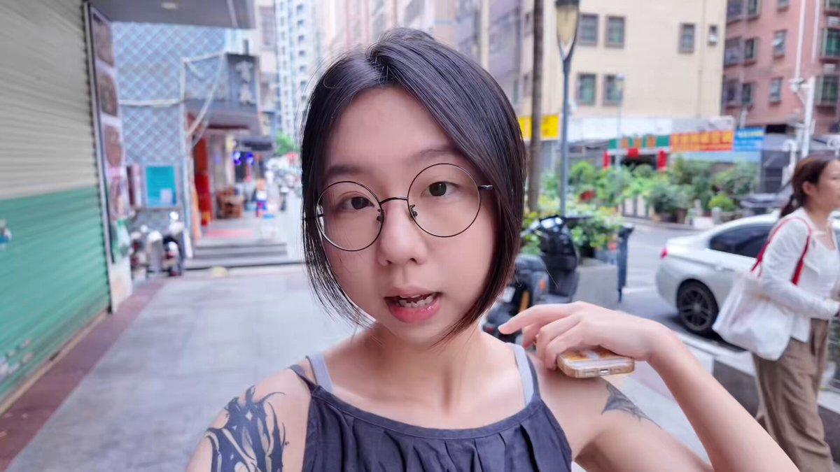 The image features a woman wearing glasses, holding her arm up with a cell phone attached to it. The photo appears to be taken by someone else who has posted it online. The caption of the image reads "Crypto Survival Plan| Day 11 《鼠鼠日记》 今天憋了波大的VLOG 长达三分钟的视频加1G的内存 走过路过不要错过 看看我一天的生活都在干什么。". The image seems to be related to the post, as it features a woman with glasses and a cell phone.