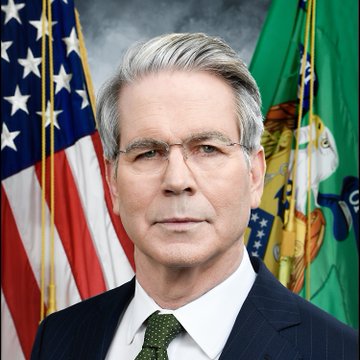 An official portrait of a man in a dark pinstripe suit with a green tie, standing in front of an American flag and a green flag with an emblem.