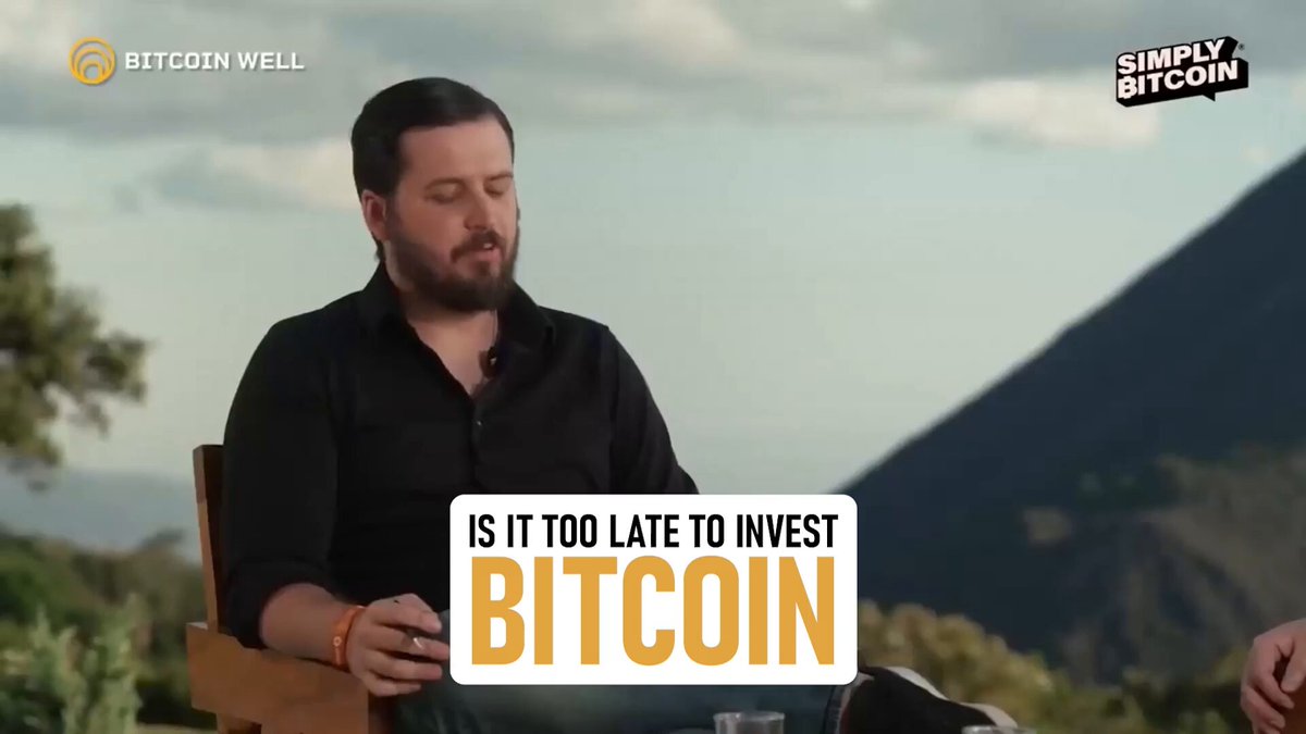 The image features a man sitting in a chair, holding a small object that appears to be a Bitcoin wallet or keychain. The background of the image shows a mountain range with trees visible behind him. Below the image, there is text that reads "Is it too late to invest Bitcoin?".