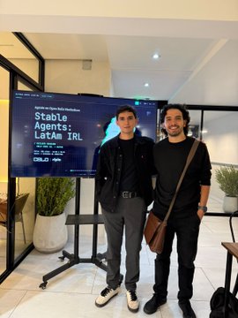 Two men pose beside a presentation screen at an IRL workshop for the “Stable Agents: LatAm IRL” track, part of the Agents on Open Rails Hackathon. The post highlights demos and support for 350+ builders across six cities, with submissions due by 11/9.