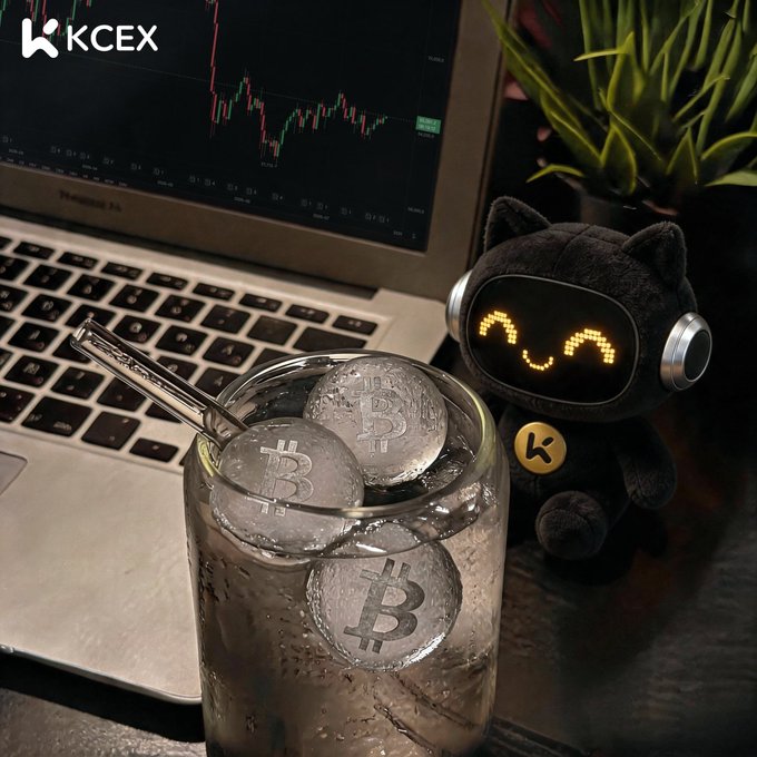 A cozy desk scene featuring a glass of ice water with Bitcoin tokens, a KCEX-branded cat plushie with glowing eyes, and a laptop displaying candlestick trading charts—visually echoing the post's message to take a break and hydrate instead of obsessively watching the charts. The KCEX logo appears in the top-left corner of the image.