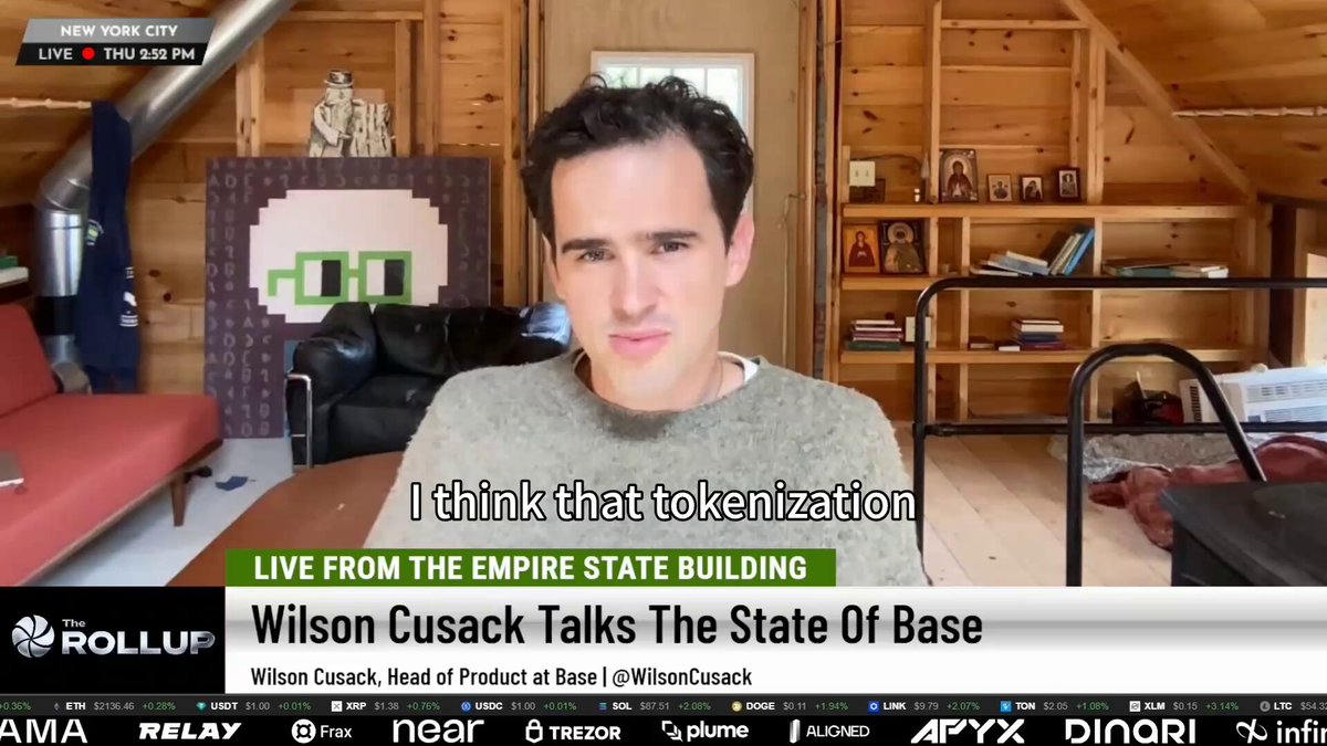 The image shows a man sitting at a table, with a TV screen behind him displaying an article about tokenization of assets. The text on the screen reads "I think that tokenization is going to be @base", which suggests that the content being displayed is related to the concept of tokenizing various asset classes in the financial world.