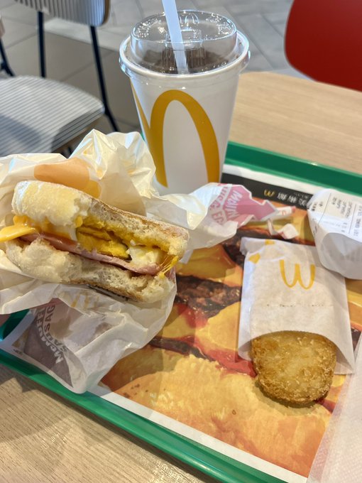 The image shows a McDonald's meal consisting of a sandwich, chips, and a drink placed on a tray at a table. The tray also contains a receipt for the order. A straw can be seen next to the drink, but it appears that the straw is no longer available or in use due to its discontinued status.