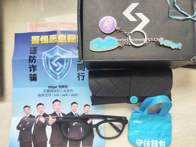 The image features a collection of items, including a pair of glasses, a keychain with a picture of a man holding a gun, and some other objects such as a wallet and a book. The post includes text that reads "哈哈 刚打开周边的时候", which is likely related to the items in the image. The post also mentions a website called Bitget, possibly indicating that some of these objects are related to Bitget or have been purchased using Bitget's services.