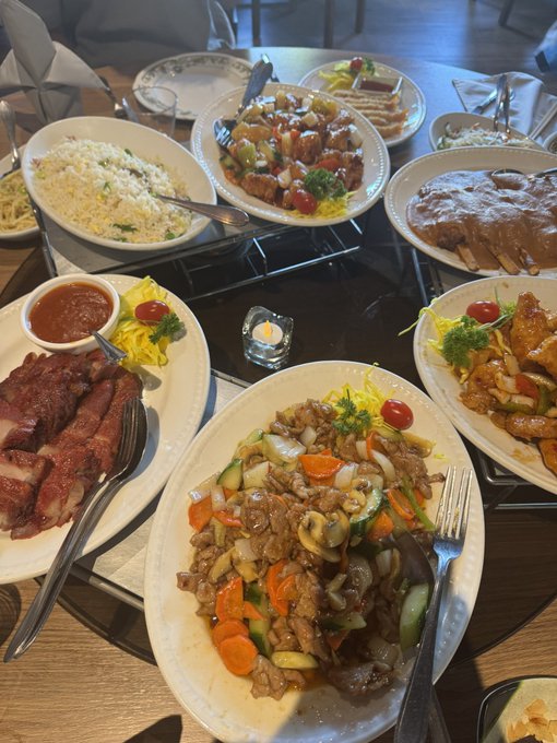 A table spread of various Chinese dishes including fried rice, char siu, beef and vegetable stir-fry, and other plates with sauces.