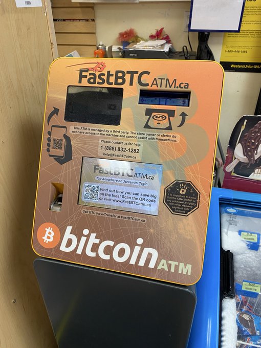 An orange FastBTC ATM.ca bitcoin machine stands indoors, displaying a QR code, contact number 1-888-832-1282, and various sponsor logos.