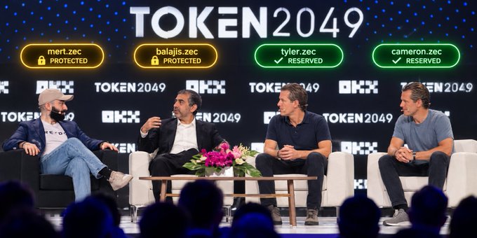 Four men participate in a panel discussion at the TOKEN2049 conference, with background graphics showing domain names like 'tyler.zec' and 'cameron.zec' marked as RESERVED.