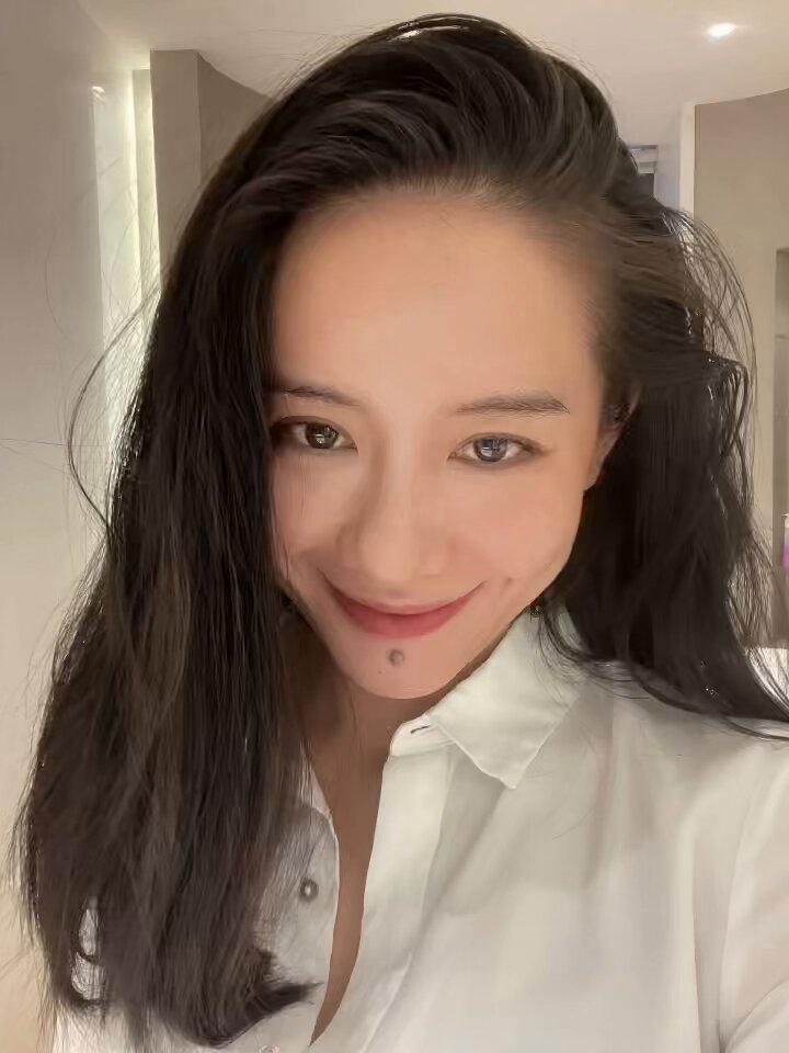 The image features a woman with long brown hair wearing a white shirt, smiling at the camera. The caption of the photo reads "一直说不出来何一的美感来自哪里", which is likely an inside joke or reference to something humorous that happened between her and someone else in the image.