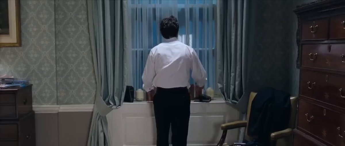 A man wearing a white shirt stands in front of a window, gazing out at something outside. The room features a bed, chair, dresser, desk with a lamp, and an art piece hanging on the wall. A caption indicates that someone has won $50k through a Polymarket TSLA Up/Down market. The post suggests that the man is a trading enthusiast celebrating his win or contemplating what he can do next with the money.