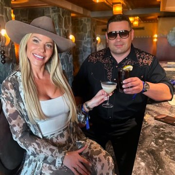 A smiling couple poses in coordinated western-style attire, with the woman in a cowboy hat and patterned dress and the man in a black embroidered western shirt, raising cocktail glasses together in what appears to be a rustic lodge setting. The image complements the post about a productive week at the SALT Conference in Jackson Hole, capturing the "excessive western wear" vibe while celebrating a toast, possibly to Canary Funds' upcoming projects.