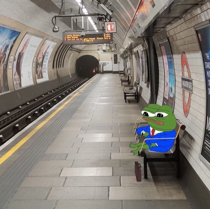 A London Underground (Bakerloo line) station platform with a cartoon Pepe the Frog in a blue suit and red tie sitting on a chair holding a cane, with a briefcase on the floor beside him.