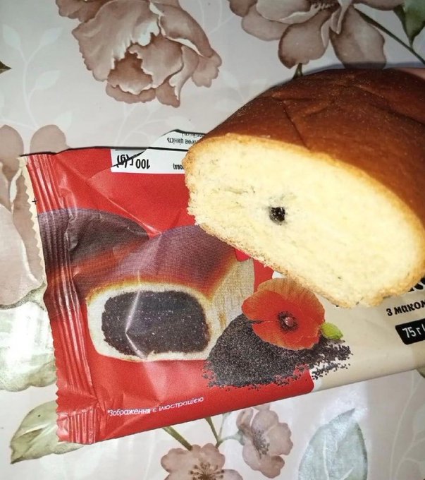 A partially eaten poppy seed bun (with packaging showing "100г" and "изображение с мастерандо") sits on a floral tablecloth, the empty crumb center resembling a "claimed" airdrop while the dark seed-filled wrapper illustrates the rewards that have already been scooped up—just like the fleeting nature of crypto airdrops.