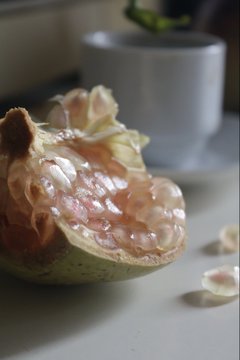 A close-up photograph shows a halved cherimoya or custard apple, revealing its white, pulpy flesh with embedded seeds, sitting on a table near a plant pot.