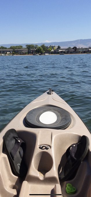 The image shows a first-person view from a kayak on a lake, with the bow pointing toward a distant shoreline of trees and houses. The post's caption "My favorite day" likely refers to the kayaking activity, suggesting it was the highlight of the fitness challenge. No visible text, numbers, or names appear in the image itself.