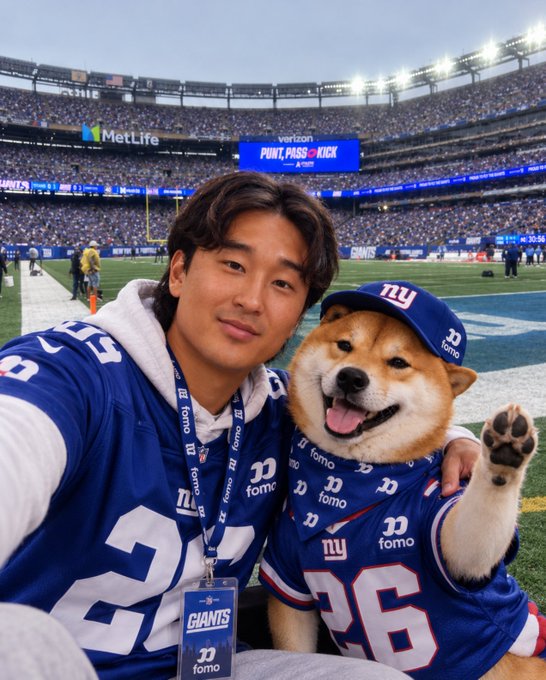 A man and a Shiba Inu dog posing together at MetLife Stadium, both wearing blue New York Giants jerseys with 'fomo' branding and 26 numbers, with the stadium crowd and 'PUNT, PASS & KICK' signage visible behind them.