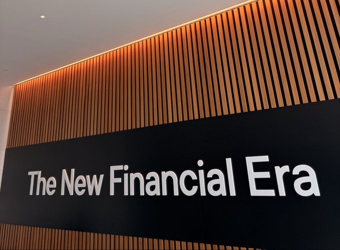 An interior photo of a wall with vertical wooden slats and warm lighting above a black sign reading 'The New Financial Era' in white lettering.