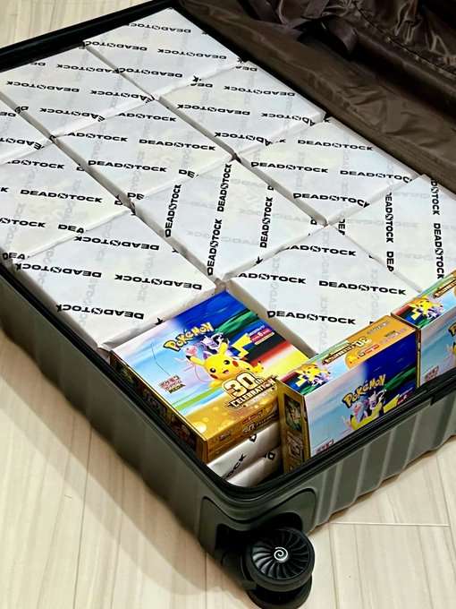 An open suitcase packed with white 'DEADSTOCK' labeled boxes along with several Pokémon trading card game products, including a 30th Anniversary collection box.