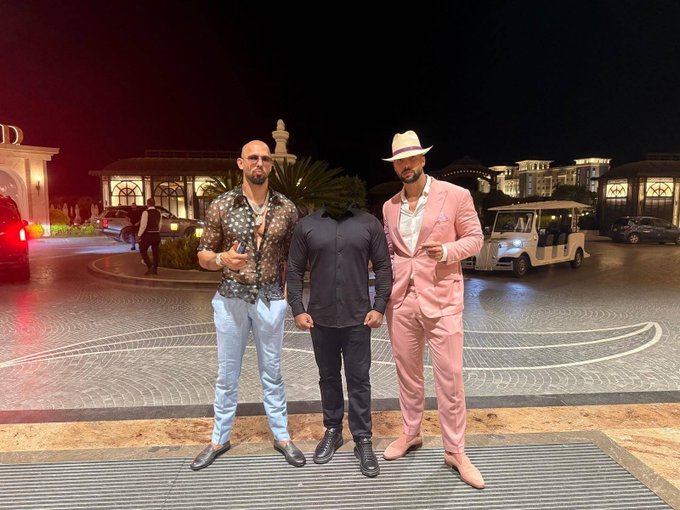 Three men pose together at night in front of an upscale entrance, with one in a bold pink suit and fedora, another in a floral shirt, and the third in a dark button-up standing between them.

The post's caption "It's not a conspiracy anymore…" pairs with the image to suggest the gathering is a public, undeniable meeting—likely featuring high-profile figures now openly seen together, reinforcing that whatever was once rumored is now visibly happening.