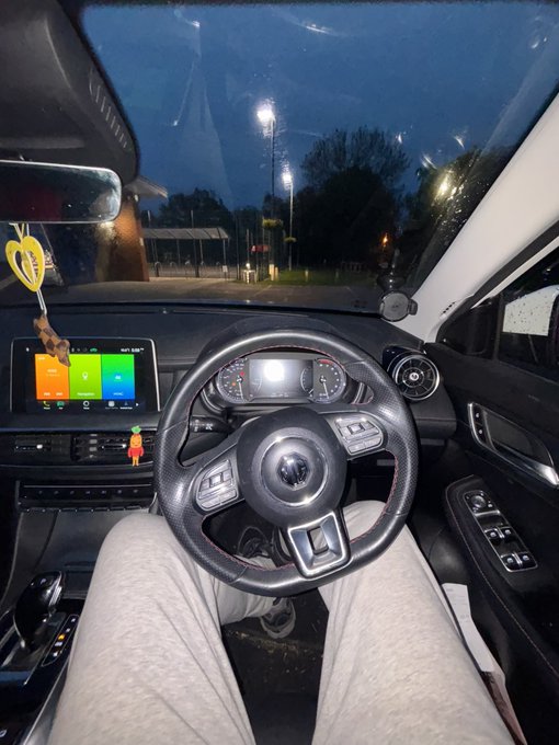 Interior view from the driver's seat of a Volkswagen car parked at night, with an illuminated dashboard and a heart-shaped ornament hanging from the rearview mirror.