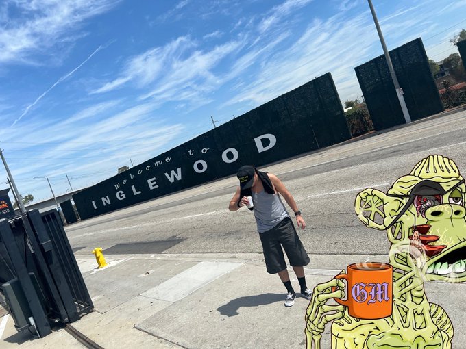 A man in a grey tank top dances on a sidewalk in front of a green wall reading 'Welcome to INGLEWOOD', with an animated zombie holding an orange 'GM' mug overlaid on the bottom right.