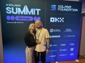 The image features a man and woman standing next to each other against a blue backdrop with white text that reads "My first summit was an absolute banger @SuperteamDE was cooking hard, what an event!". The couple appears to be posing for a photo in front of a banner or sign displaying the name of the summit.