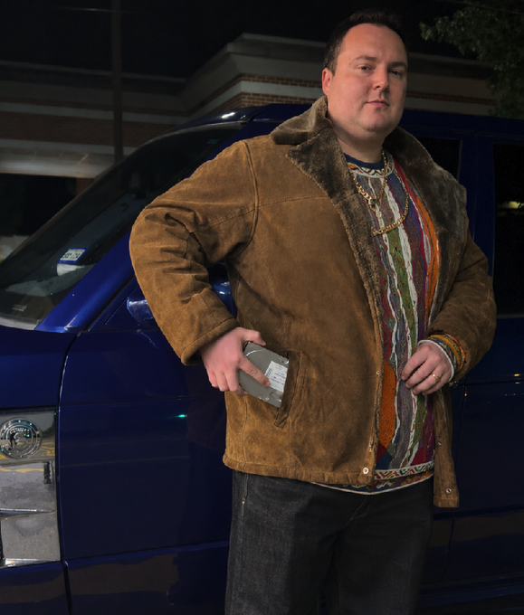 A man in a brown suede jacket and gold chain poses in front of a blue van at night, holding what appears to be a packaged product, fitting the meme's "shady back-alley deal" aesthetic for scoring a hyped AI model drop.
