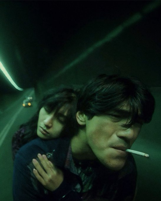 Two young people ride together through a dimly lit tunnel bathed in eerie green light, the man smoking a cigarette while the woman rests her head against his shoulder. The moody, atmospheric scene evokes a cinematic sense of late-night risk-taking, mirroring the post's reckless bullish energy about crypto investments.