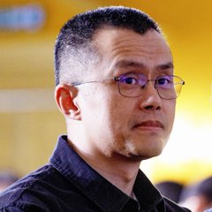 A close-up photo of CZ (Changpeng Zhao), the former CEO of Binance, wearing glasses and a dark shirt, looking off-camera with a serious expression. The image accompanies a news update about CZ discontinuing use of his public wallet due to an influx of unsolicited meme coins, despite traders using his wallet activity for profitable signals.