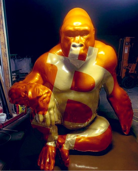 A statue of a muscular ape covered in an orange and white pattern featuring the letter 'S'.