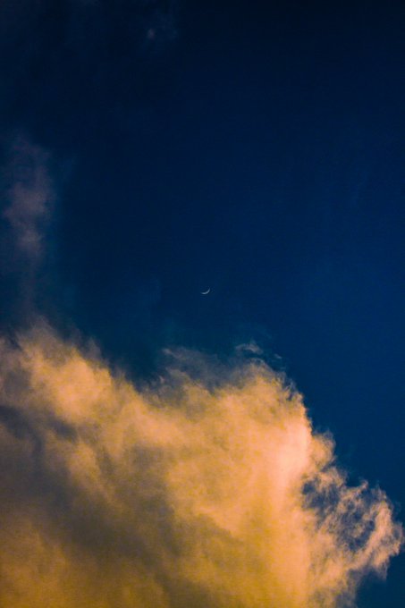 A dark blue twilight sky featuring a delicate crescent moon and large golden-lit clouds in the lower portion of the frame.