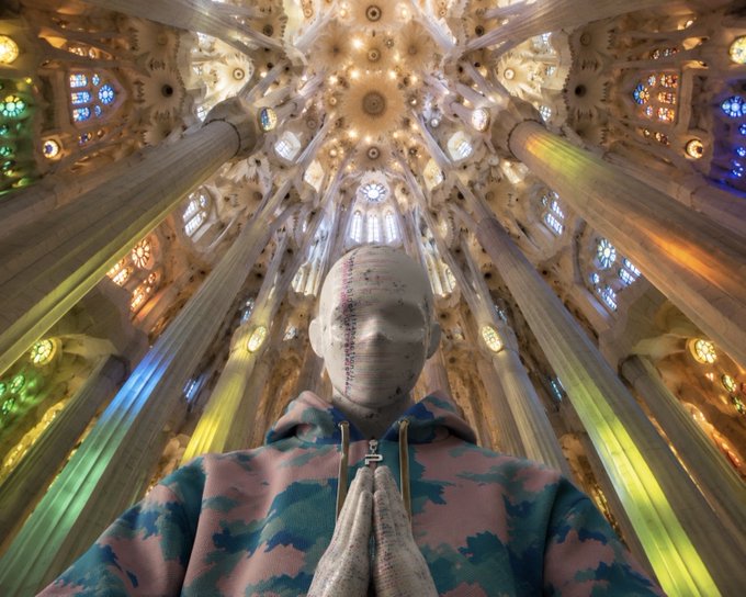 A figure with a face composed of text or code, hands clasped in prayer, stands beneath the soaring, kaleidoscopic domed ceiling of Gaudí's Sagrada Família, with vibrant stained-glass light filtering through the ornate columns—merging sacred architecture with a digital, AI-crafted surreal aesthetic that resonates with the post's call to psychonauts, AI creatives, and crypto enthusiasts drawn to transcendent, otherworldly imagery.