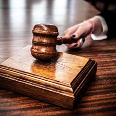 A hand reaches to lift a wooden gavel atop a polished sound block, evoking the ruling power of a courtroom. The image visually reinforces the news that the Ninth Circuit Court has decided Kalshi, Crypto.com, and Robinhood's sports event contracts aren't "swaps."