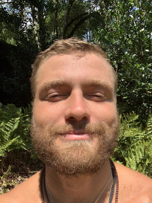 A close-up selfie of a bearded man with closed eyes, smiling peacefully in a lush, green forest setting with sunlight filtering through ferns and trees—evoking a serene, transcendent connection to nature that aligns with the spiritual "cognisphere" theme of the #spx6900 post.