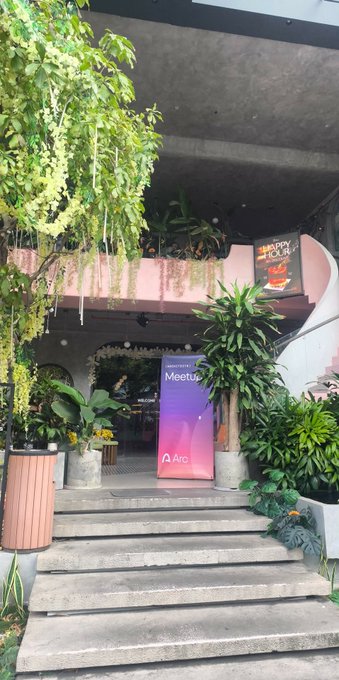 A staircase leading up to a building entrance labeled 'Meetup' with an Arc logo, surrounded by lush green plants and hanging vines.