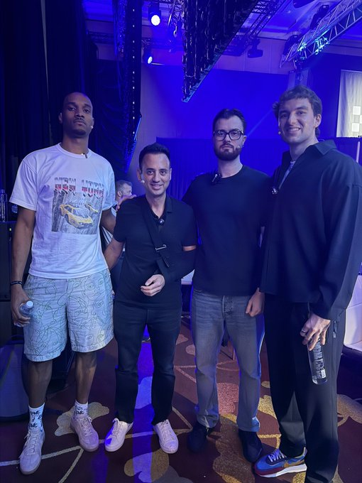 Four men pose for a photo at what appears to be a blue-lit industry event or conference, with one wearing a t-shirt featuring Hebrew text and a race car graphic, while another holds a water bottle. The casual gathering seems to relate to a candid discussion about the volatile nature of memecoins, reflecting the post's sentiment about the gambling-like nature of these tokens despite the surprising longevity of major ones such as Doge and Pepe.