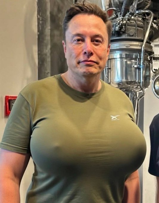 Elon Musk wearing an olive-green SpaceX t-shirt stands in front of what appears to be rocket engine hardware.