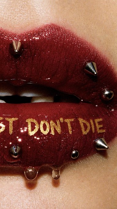 A close-up artistic photo of lips painted dark red/burgundy with gold text reading 'DON'T DIE' and silver spikes/studs, with clear liquid droplets dripping down.