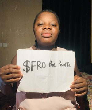 A woman holds up a hand-lettered sign reading "$FRO the People," visually echoing the post's call to recognize $FRO before it gains mainstream attention. The image reinforces the message about backing under-the-radar projects, tying into the post's question about what drew attention to the $FRO coin and its creator @ogafroman.