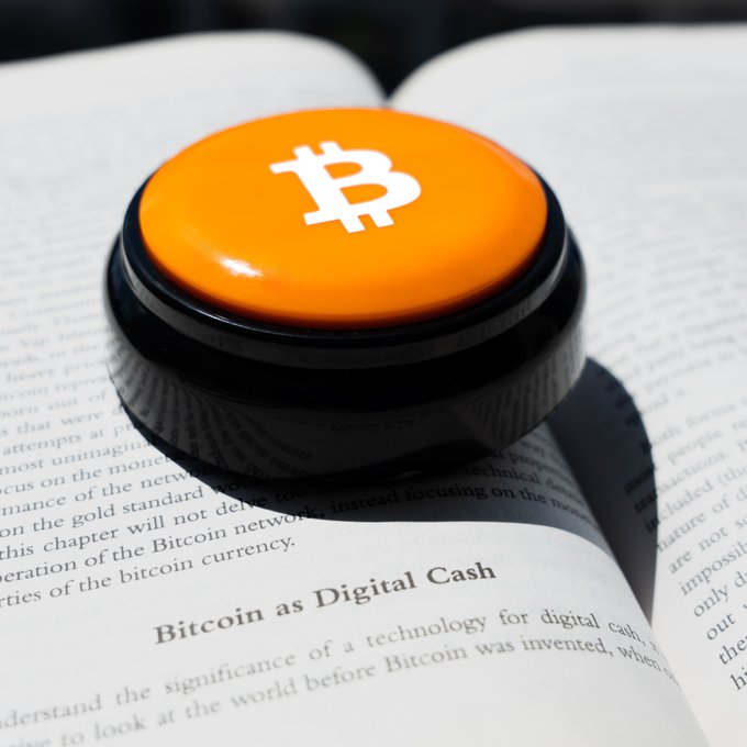 A glossy orange Bitcoin-branded button rests atop an open book displaying the chapter heading "Bitcoin as Digital Cash," visually translating the post's "Bitcoin Easy Button" metaphor into a tangible "tap into instant bull mode" moment.