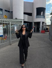 A stylish woman poses with two peace signs in front of a building entrance, dressed in a black blazer and pants with sunglasses. The image appears to promote an upcoming live interview on X at 7 PM EST featuring Alex "Shillin Villain" @Shilllin in an unscripted crypto conversation.