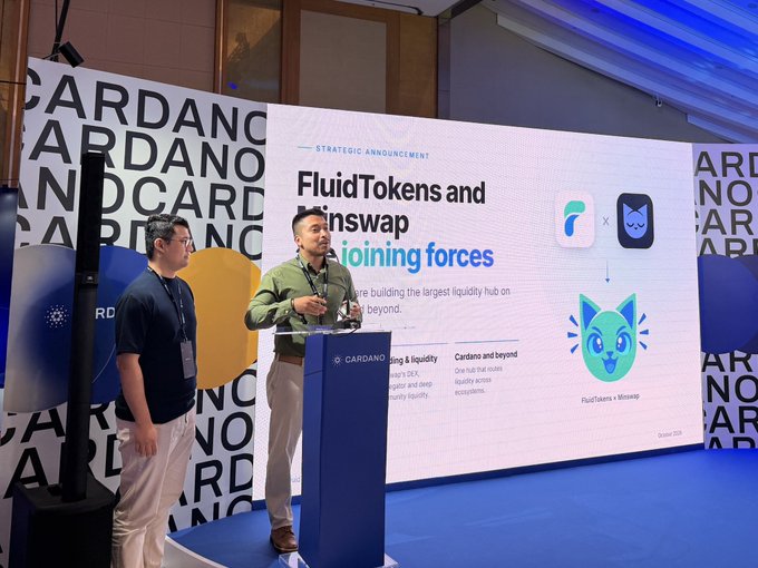 Two men present on stage at a Cardano conference, standing beside a podium with a presentation screen behind them reading 'STRATEGIC ANNOUNCEMENT: FluidTokens and Minswap - Cardano and beyond' with a 'FluidTokens x Minswap' logo.