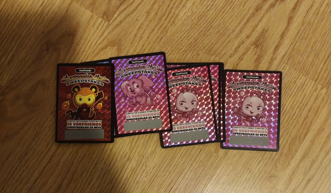 Four Neopets 'Sweepstakes' collectible game cards, three pink and one red, are spread out on a wooden table.