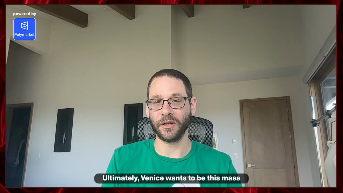 The image shows a man wearing glasses sitting at a desk, with a computer screen behind him displaying a message about a video game called "Ultimate Venice wants to be this mass". The man appears to be engaged in playing the game or discussing its features with someone else who is not visible in the frame.