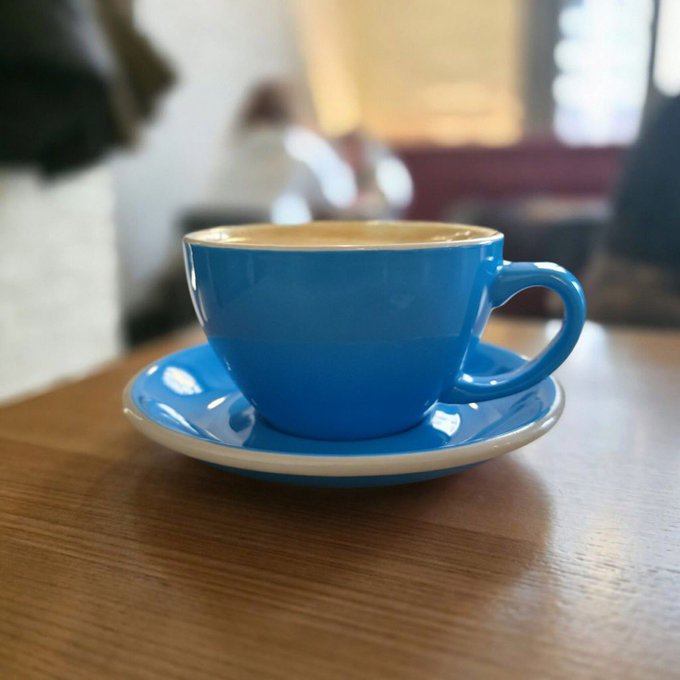 A vibrant blue ceramic cup filled with coffee sits on a matching saucer atop a wooden table, capturing a cozy Sunday morning moment perfect for "baseposting and coffee."