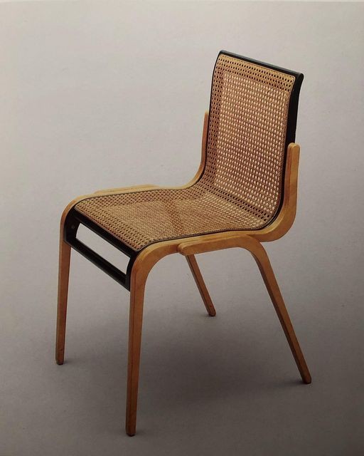 A wooden chair with a woven rattan seat and backrest sits against a plain gray background. The chair features a curved design with light-colored wood framing and splayed legs.