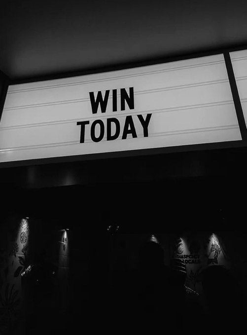 A black and white photograph of a lit marquee-style sign reading 'WIN TODAY' above a dark entryway with illuminated wall lamps.