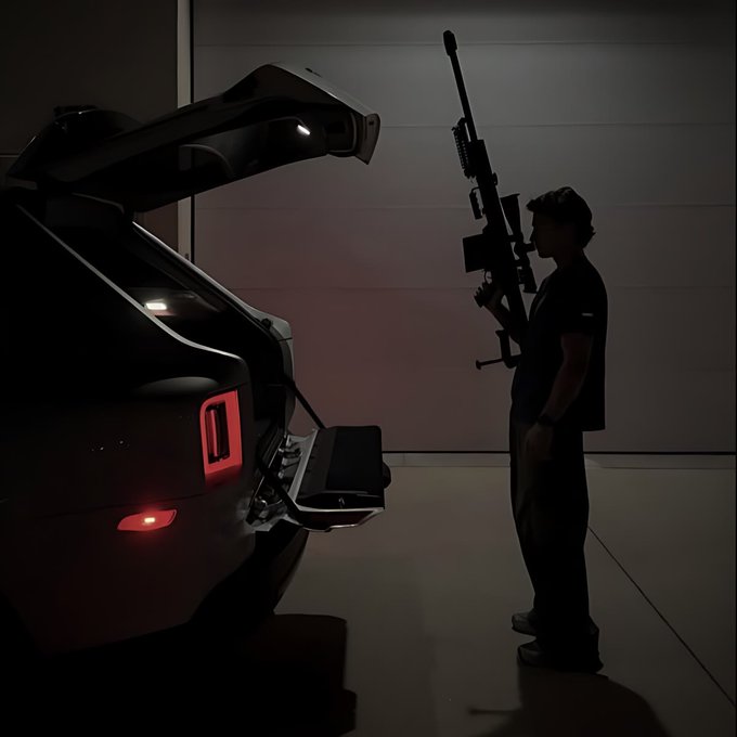 A dark silhouette image of a person holding a sniper rifle next to a sports car with its trunk open and rear lights illuminated.