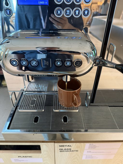 A chrome espresso machine pours coffee into a brown mug on its drip tray, with the 'LINNEO' logo visible on the top display and waste bins labeled 'PLASTIC' and 'METAL GLASS BIOWASTE' below.