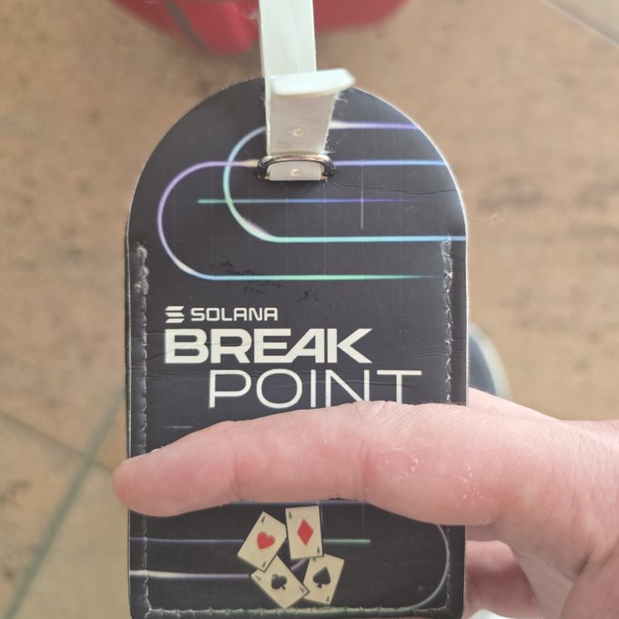 A hand holds a black Solana 'Break Point' lanyard badge featuring neon curved lines and small playing card icons at the bottom.