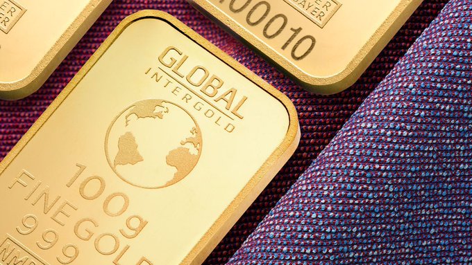 Gold bars labeled "GLOBAL INTERGOLD," "100g FINE GOLD," and "999.9" rest on a purple fabric, visually symbolizing the long-term value reserve described in the post about Artrade's 85,000,000 $ATR DAO Long Term Reserve dedicated to protocol expansion.